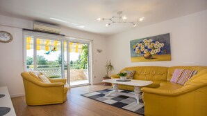A bright living room with yellow furniture, a painting of flowers, and a view through a glass door. - Beautiful Apartment in Prime Location (Porec)