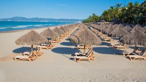 Una spiaggia con file di lettini e ombrelloni di paglia, un cielo azzurro limpido e un mare calmo.