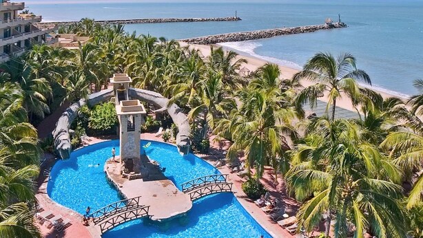 Un resort con una grande piscina circondata da palme e una spiaggia.