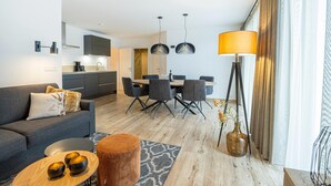 A modern living room with a sofa, coffee table, and ottoman. There is a dining area with a table and chairs. The room has a large window with curtains and a floor lamp. - Apartment in Salzburg Near Schlossalmbahn I (Bad Hofgastein)