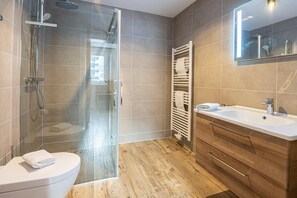 Een moderne badkamer met een douchecabine van glas, een wit toilet en een houten wastafelmeubel met een wastafel.