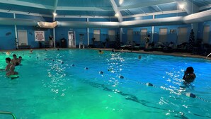 An indoor swimming pool with clear lanes, a lifeguard station, and a blue ceiling.