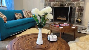A living room with a teal sofa, a white vase with flowers, a round wooden coffee table, and a fireplace with decorative items.