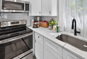 A modern kitchen with stainless steel appliances, white cabinetry, and a window with sheer curtains.