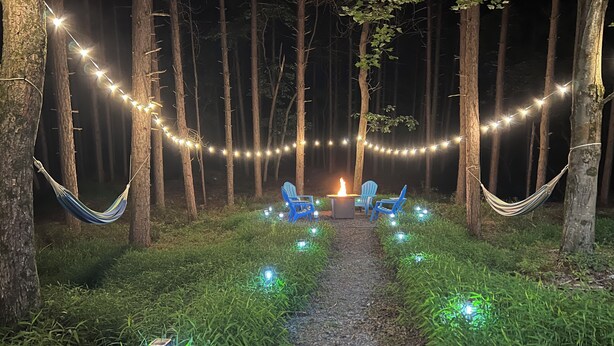 A nighttime outdoor setting with a fire pit, string lights, and hammocks.