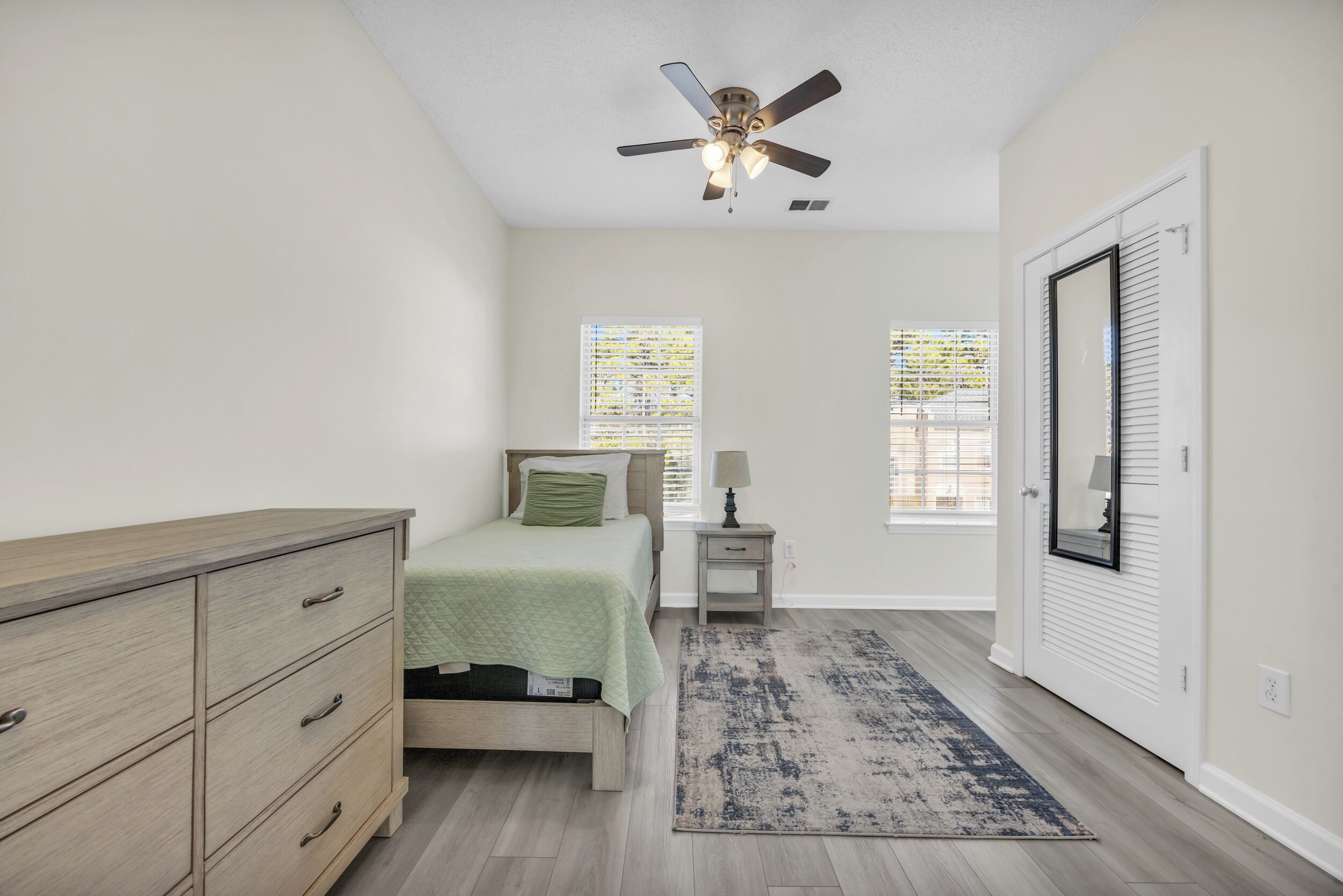 A bedroom with a bed, dresser, nightstand, lamp, and a ceiling fan.