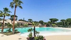 A swimming pool surrounded by palm trees and a building with arches. - Parc Oasis by Interhome (Gassin)