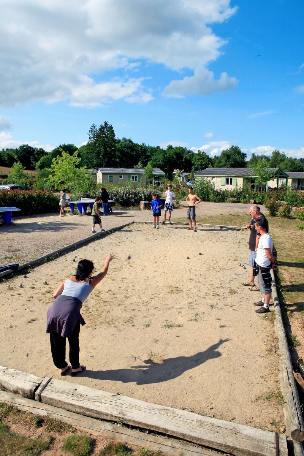A sandy outdoor area with ping pong tables and a wooden fence.