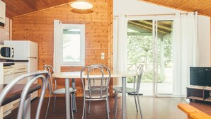 A cozy cabin with a wooden interior, a dining area with metal chairs, a small kitchen with a microwave, and a sliding glass door leading to a balcony. - Les Hameaux de Miel by Interhome (Beynat)