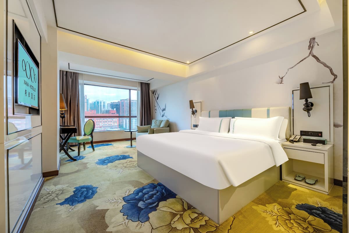 Een hotelkamer met een groot bed, een bureau, een stoel, een televisie en uitzicht op de stad.
