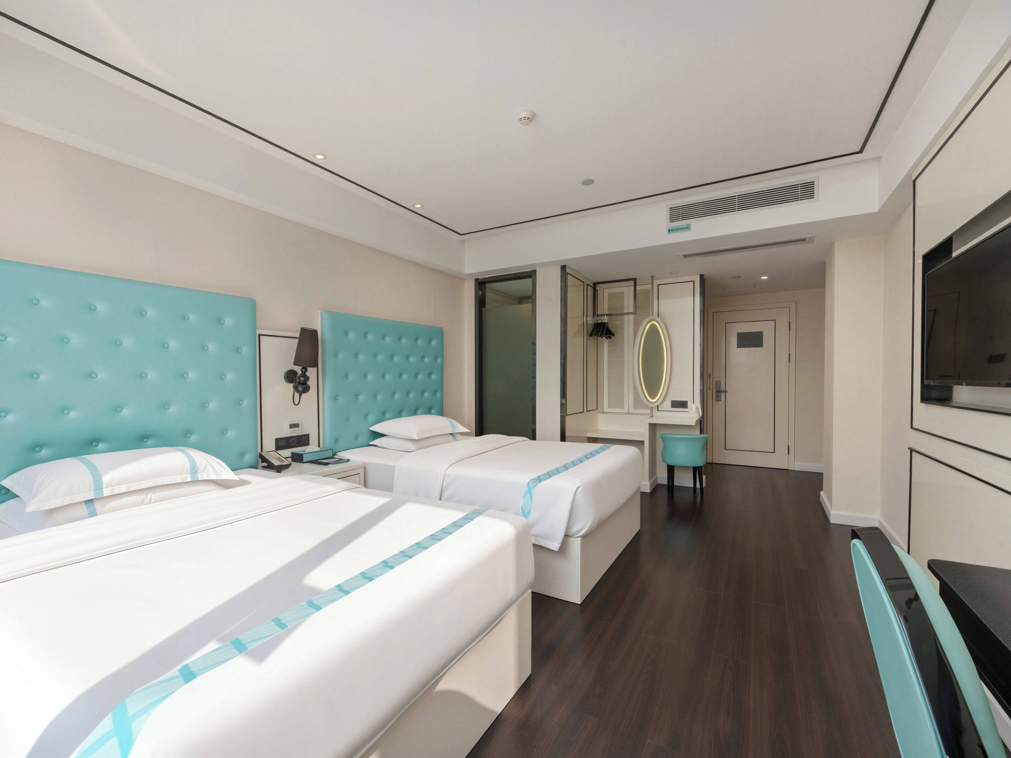 A hotel room with two beds, a desk, a mirror, and a TV.