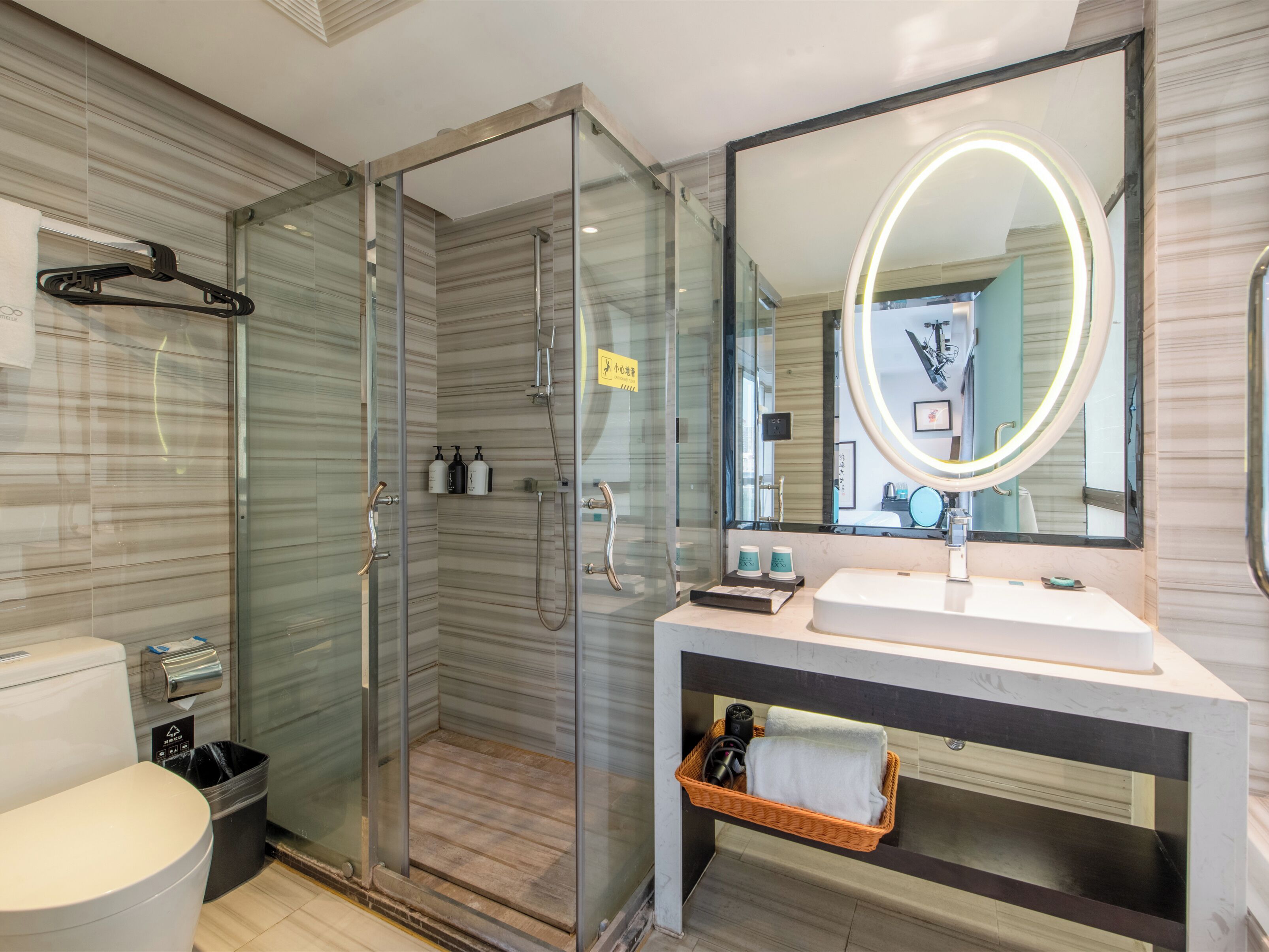 A modern bathroom with a glass-enclosed shower, a large mirror with a light, and a white sink.