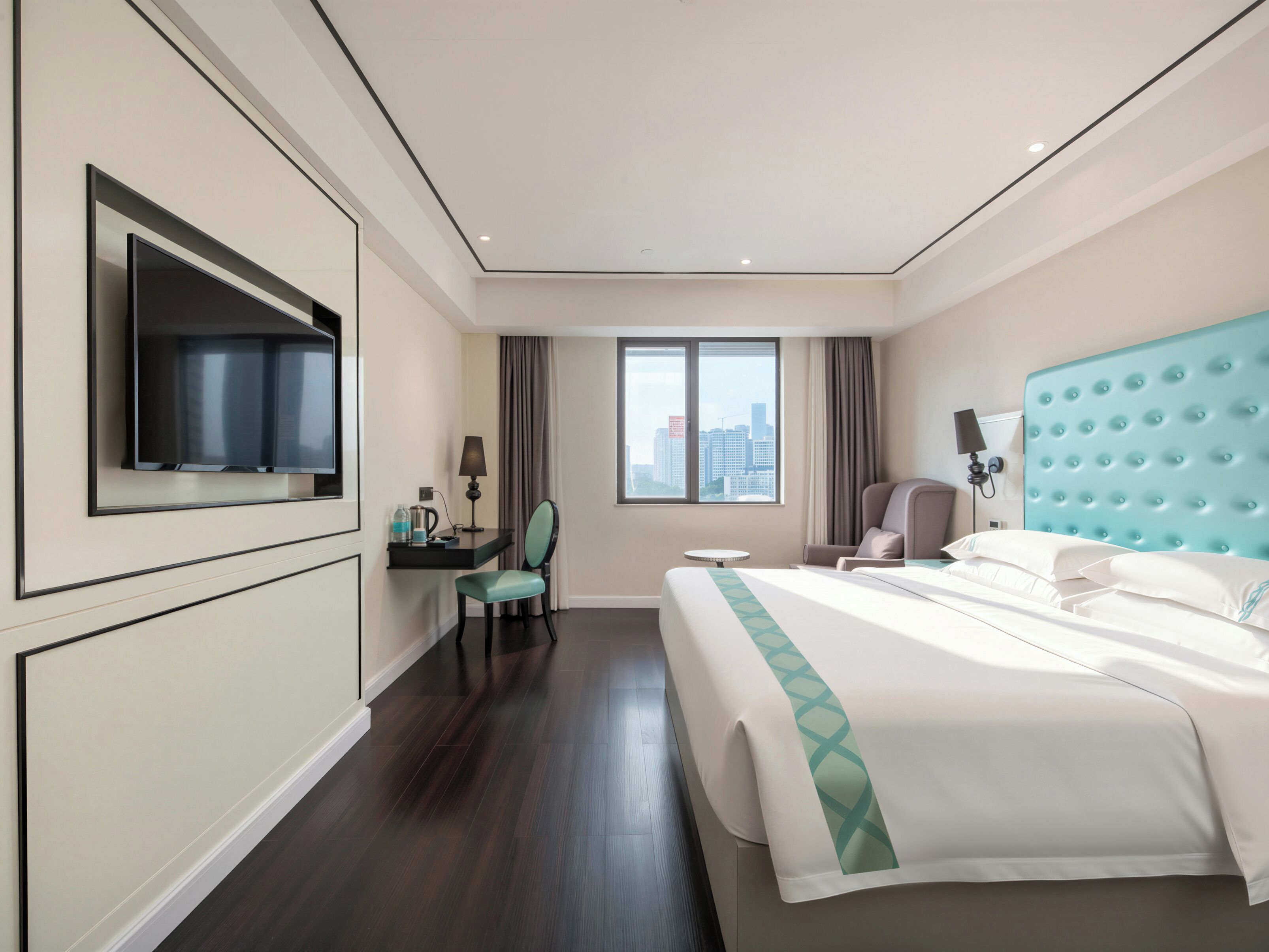 Habitación de hotel con cama, escritorio, silla, televisor y ventana con vista a la ciudad.