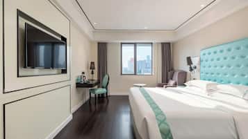 A hotel room with a bed, a desk, a chair, a television, and a window with a city view.