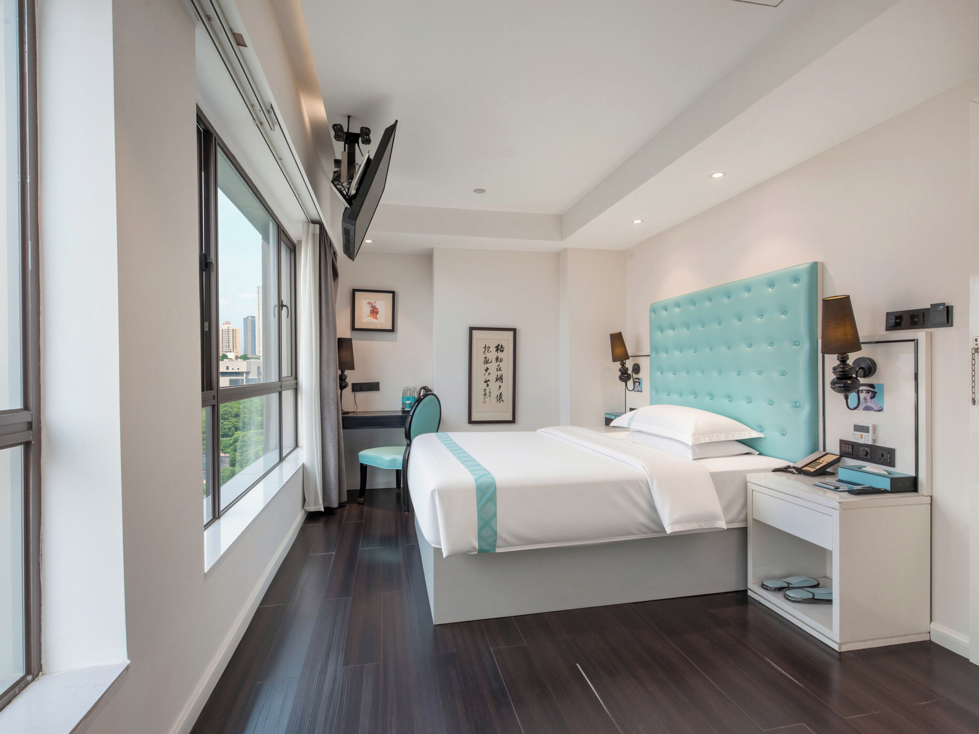 A modern hotel room with a large bed, a desk, and a view of the city.
