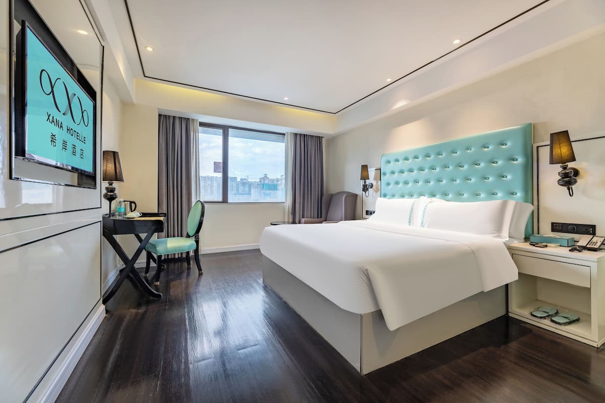 Een hotelkamer met een groot bed, een bureau, een stoel, een televisie en een raam met uitzicht op de stad.