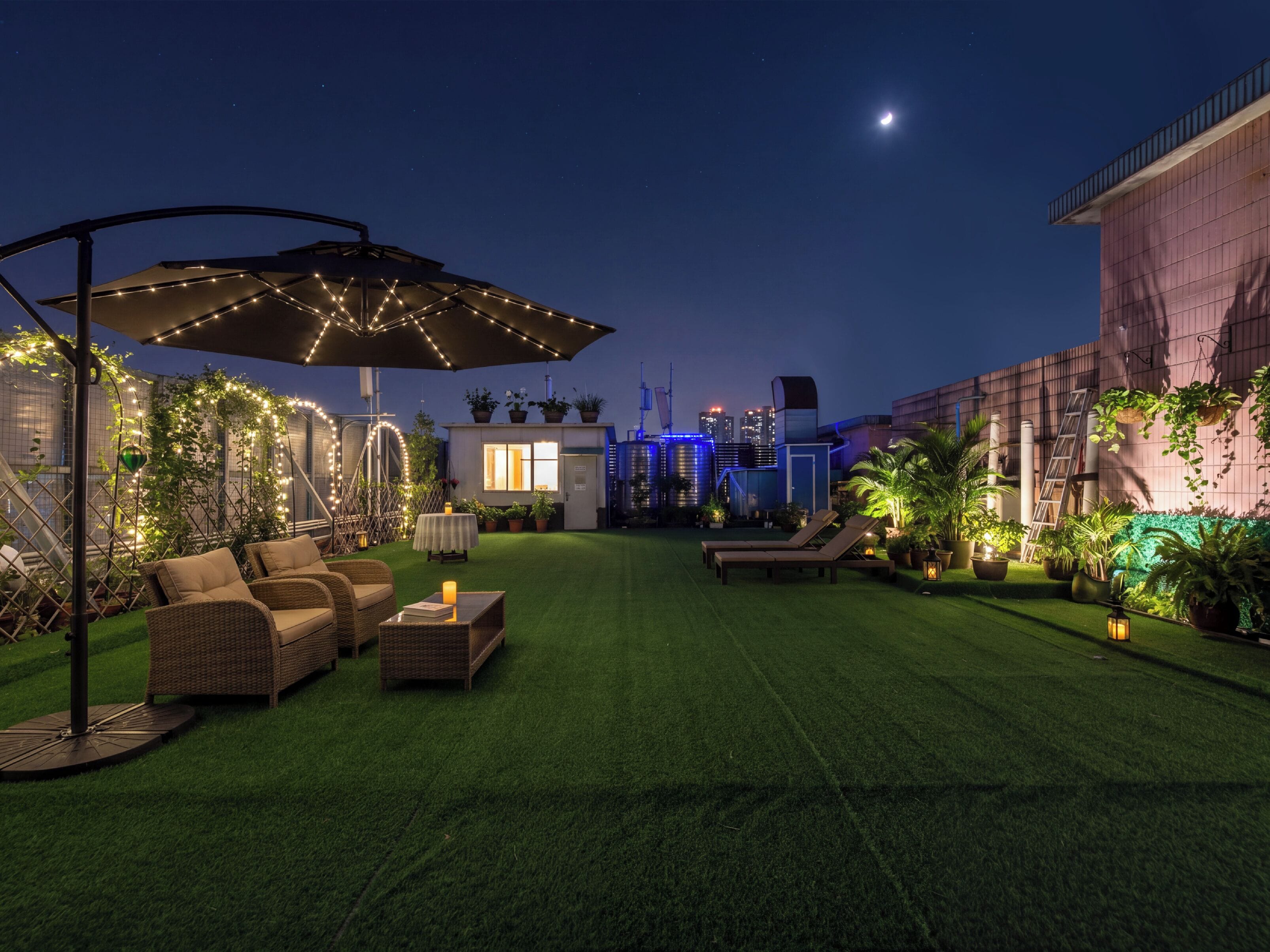 A rooftop garden with artificial grass, outdoor furniture, and string lights.
