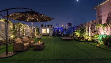 A rooftop garden with artificial grass, outdoor furniture, and string lights.