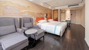 A hotel room with a sofa, a small round table, two beds, and a wall with traditional artwork.