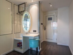A modern bathroom with a vanity, a mirror with lights, a blue chair, and a door. - XANA LITE Hotel Shixi Metro Station (Guangzhou)