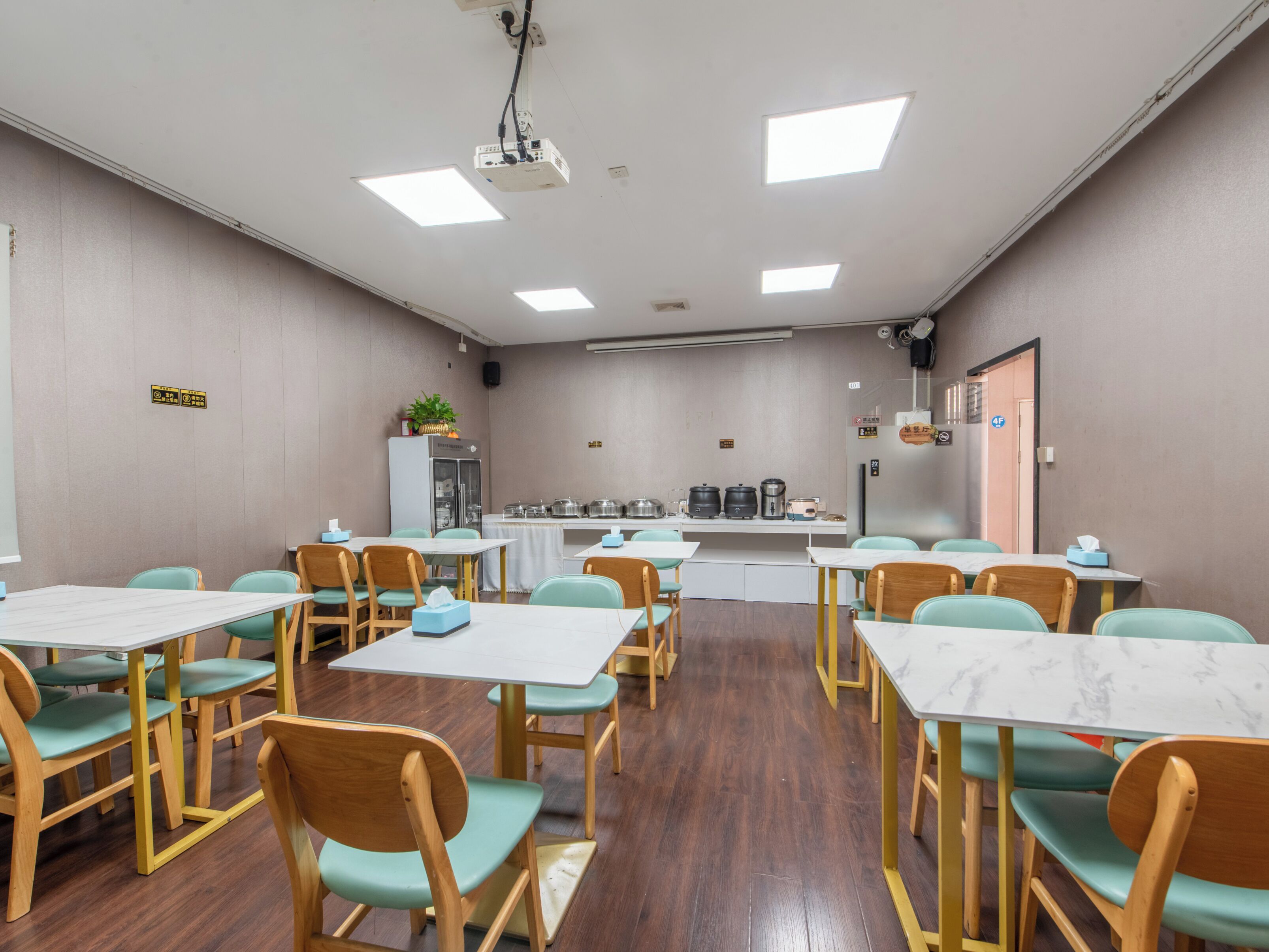 A conference room with tables and chairs, a projector, and a refrigerator with food items.