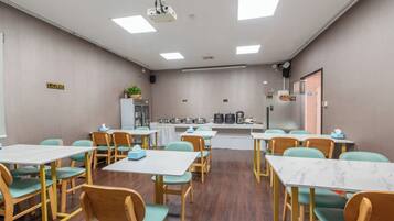 A conference room with tables and chairs, a projector, and a refrigerator with food items.