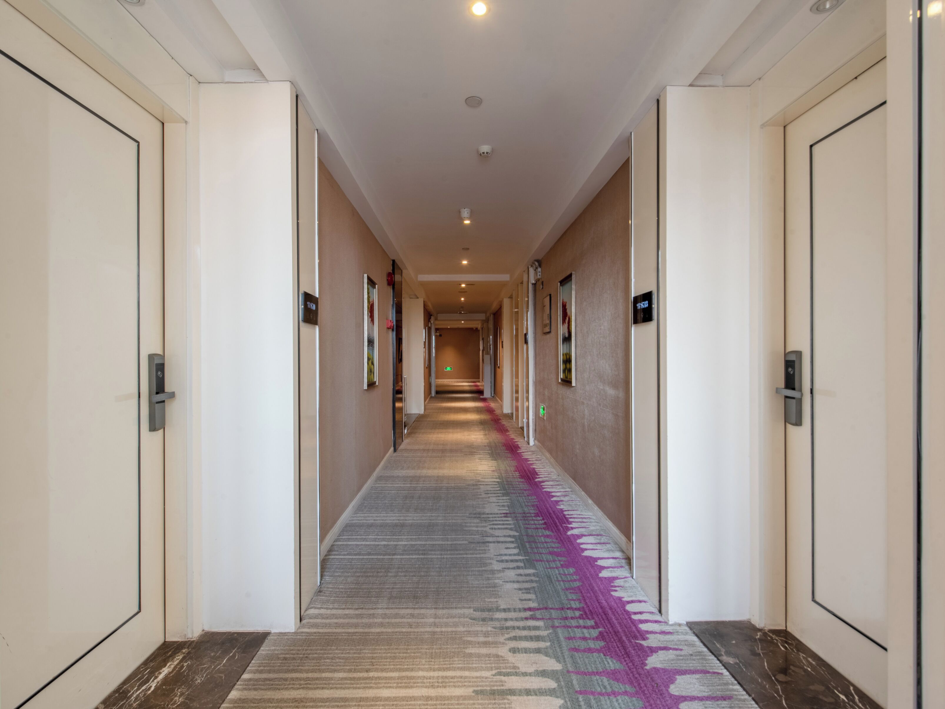 A hotel hallway with doors on both sides, a patterned carpet, and a ceiling light.