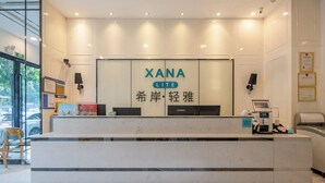 A reception desk with a sign reading 'XANA LITE' and Chinese characters, a computer, a cash register, and a chair.