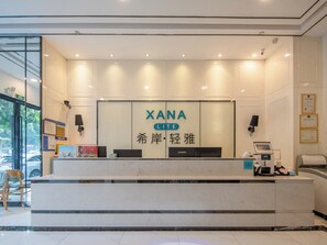 Un comptoir d’accueil avec une enseigne indiquant « XANA LITE » et des caractères chinois, un ordinateur, une caisse enregistreuse et une chaise.