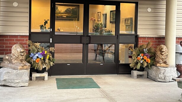 A hotel entrance with a black door, two lion statues, and a green mat. - Fairview Inn (Simcoe)