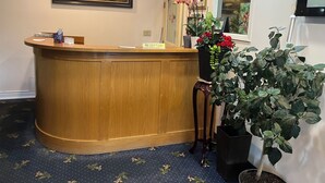 A reception desk with a wooden finish, a nameplate, and a potted plant with red flowers. - Fairview Inn (Simcoe)