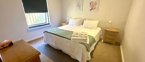 Un dormitorio con cama, dos mesitas de noche, un velador, una ventana con persiana y dos cuadros colgados en la pared.
