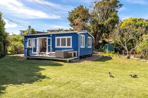 Een klein, gelijkvloers blauw huis met een veranda, een eettafel en een stoel.