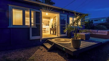 A modern house with a sliding glass door entrance, a small porch with a wooden deck, and a potted plant.