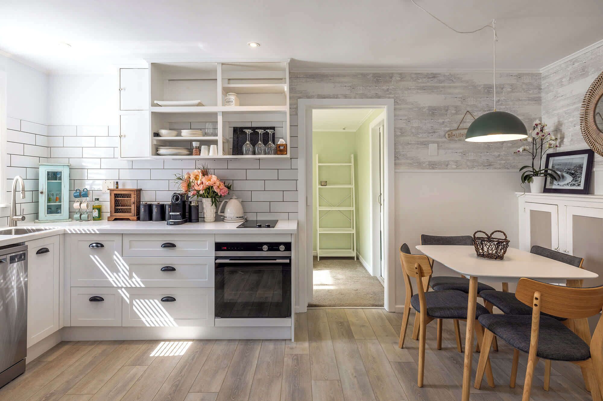 A modern kitchen with white cabinetry, a built-in oven, and a dining area with a table and chairs.