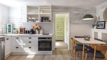 A modern kitchen with white cabinetry, a built-in oven, and a dining area with a table and chairs.