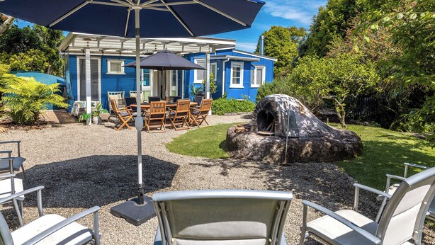 A blue house with a patio area featuring outdoor furniture and a stone oven. - Totara Cottage - Our Island (Waiheke Island)