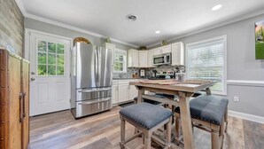 A modern kitchen with stainless steel appliances, white cabinetry, and a wooden dining table with stools.