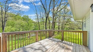 A wooden deck with a railing, overlooking a grassy yard and trees.