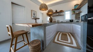 A modern kitchen with a central island, wooden bar stools, a hanging light fixture, and built-in appliances. - Seminyak 3BR Private Pool Villa (Seminyak)