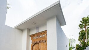 A modern building with a wooden door, a large vase, and a narrow pathway. - Seminyak 3BR Private Pool Villa (Seminyak)