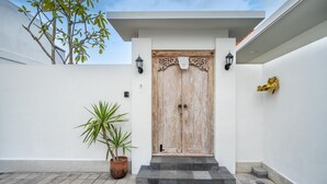 A white building with a wooden door, a potted plant, and a small staircase leading to the entrance.