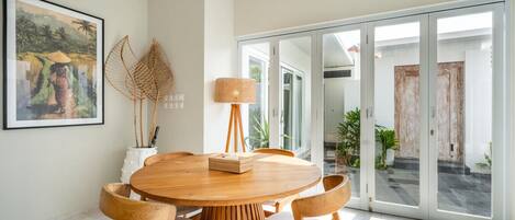 Un espace repas moderne avec une table ronde en bois et quatre chaises, un lampadaire à abat-jour en fibres tressées et un tableau encadré accroché au mur.