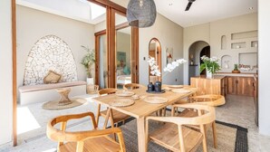 A dining area with a wooden table, woven placemats, and a hanging light fixture. - Villa Glentana - 3BR EPIC Sunset Villa (Seseh)