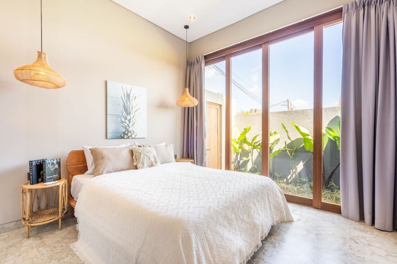 A bedroom with a large bed, two hanging lamps, a window with curtains, and a wall-mounted picture.
