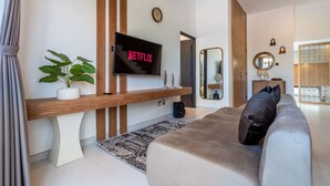 A modern living room with a flat-screen TV, a wooden bench, a sofa, a potted plant, and a decorative mirror.