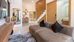 A modern living room with a sofa, a coffee table, and a TV. There is a staircase leading to another room.