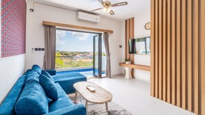 A modern living room with a blue sofa, a wooden coffee table, a TV, and a view of the city through large windows.