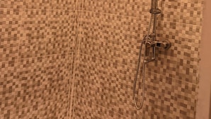 Una ducha con pared de azulejos a cuadros y cabezal de ducha manual.