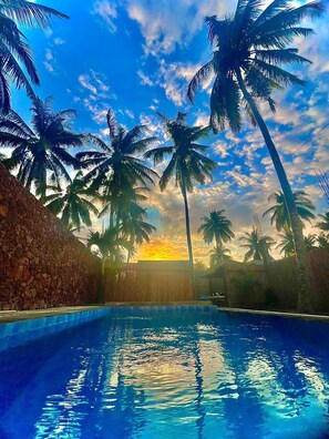 Una piscina con palmeras y un atardecer de fondo.